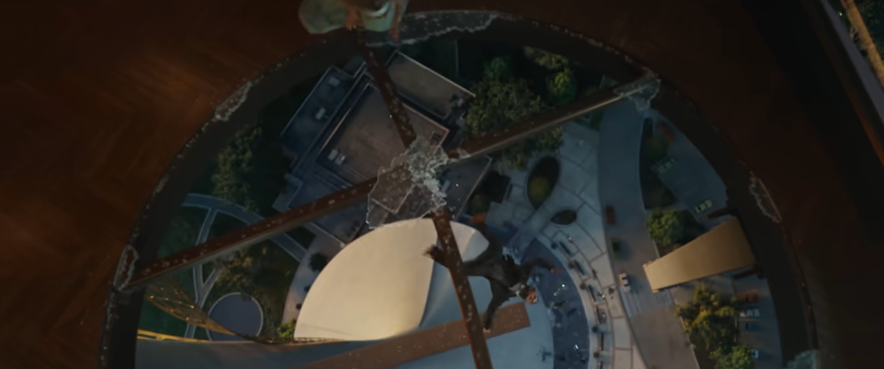 View from a tall structure looking down onto a circular plaza with buildings and trees; person at top left climbing down