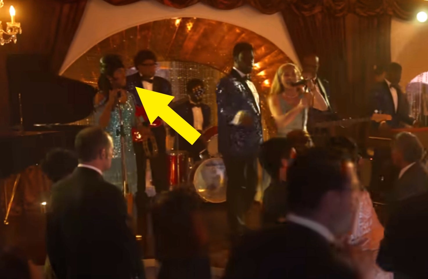 A lively ballroom scene with a band performing on stage, surrounded by elegantly dressed guests dancing and socializing