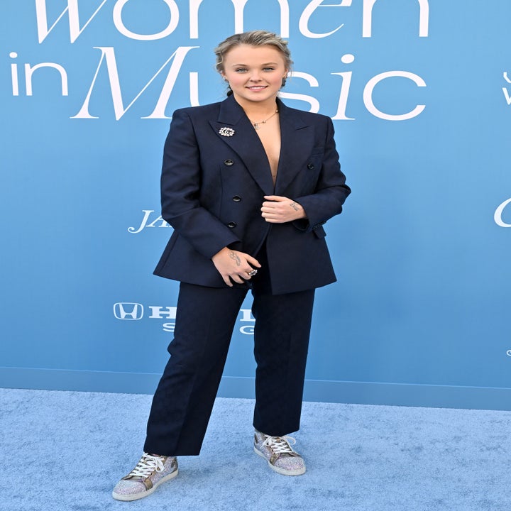 Person in a stylish suit with a double-breasted jacket and sneakers, standing in front of a "Women in Music" backdrop