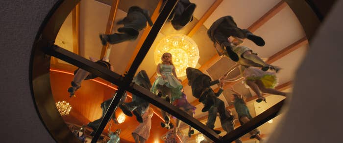 View from below of people dancing energetically on a transparent floor with a chandelier above