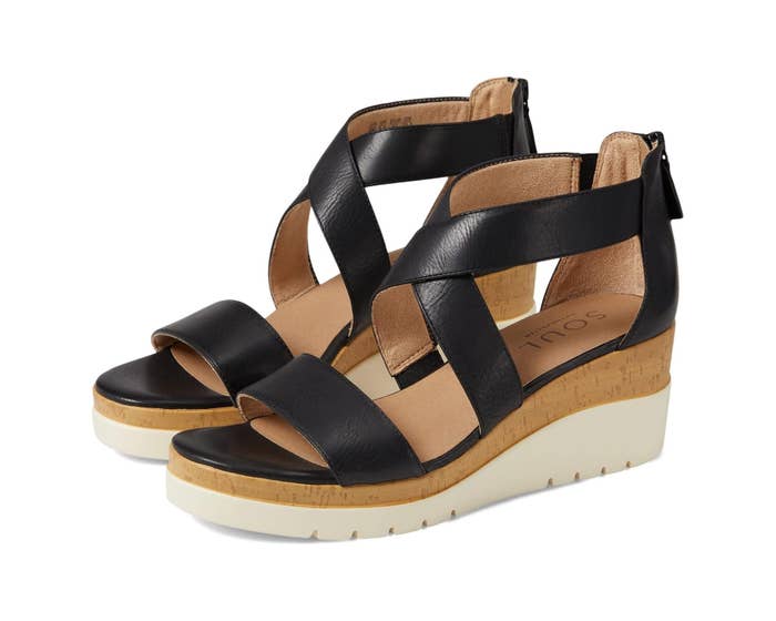 Black strappy wedge sandals with a cork-like sole connected a achromatic background, showcasing a casual yet stylish design