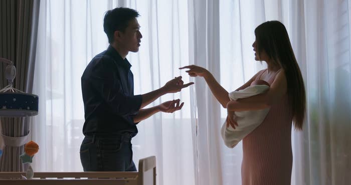 A couple, silhouetted, appears to argue near a crib; the woman holds a baby in a blanket, gesturing at the man
