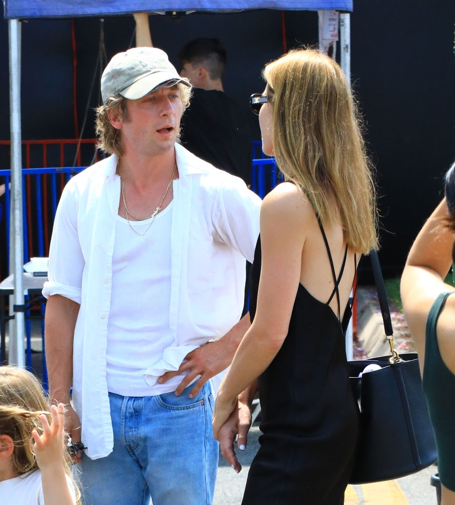 Two people talking outdoors; woman in sleeveless dress, man in casual shirt and cap. Casual setting