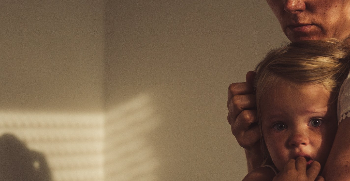 A woman embraces a child in a softly lit room, both gazing thoughtfully into the distance, creating a tender and intimate moment