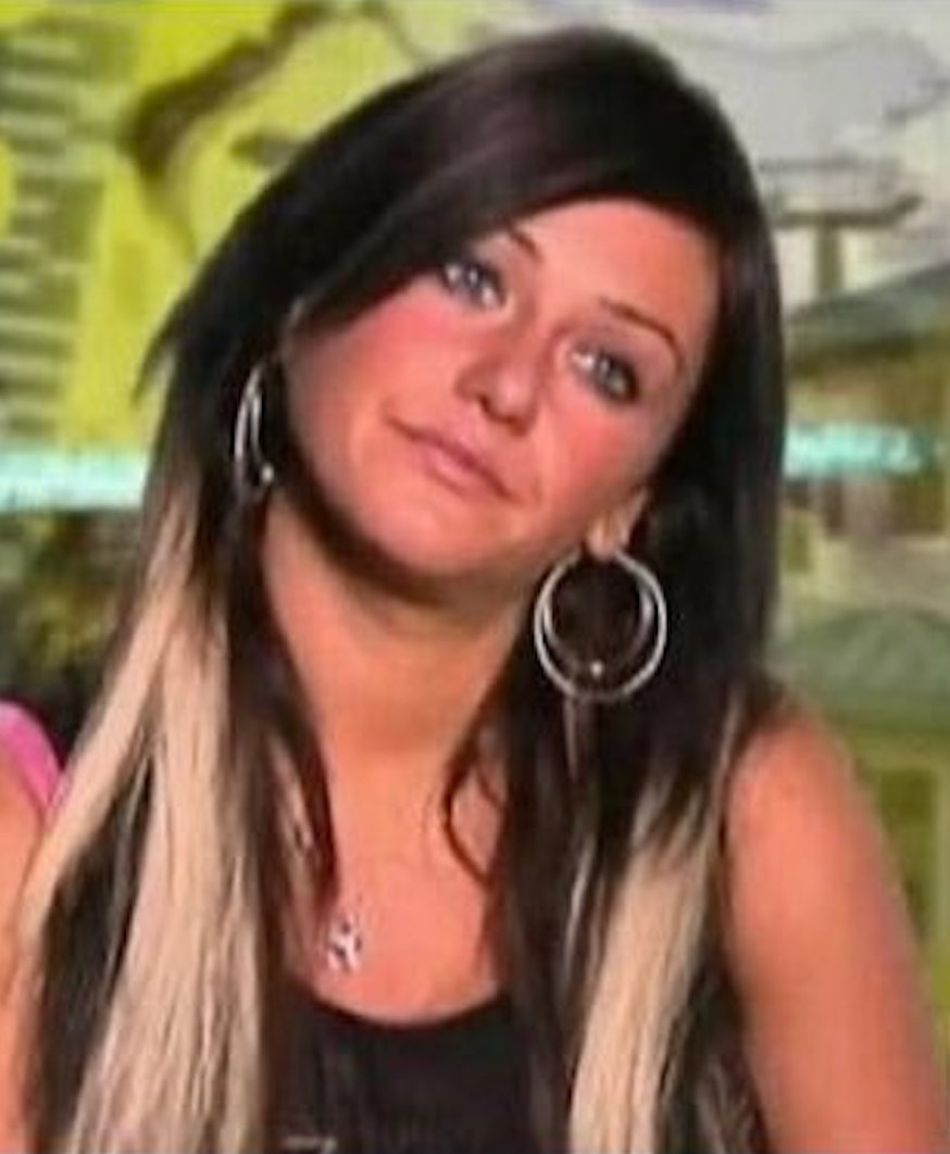 Person with long hair and hoop earrings looks at the camera with a neutral expression. Background is blurred