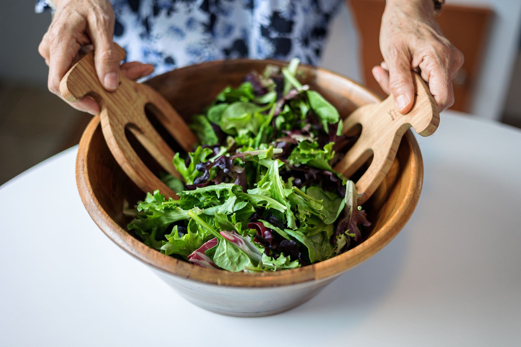Person tossing fresh salad in a wooden bowl using wooden salad servers