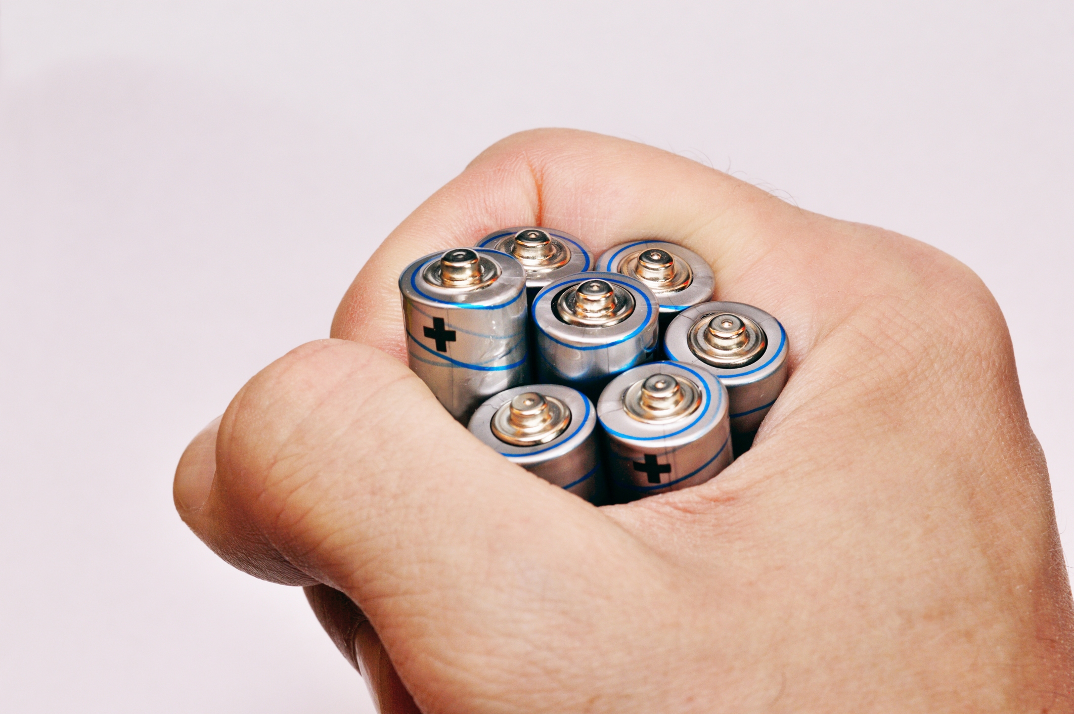 A hand tightly grips seven AA batteries, showing the tops with positive terminals visible