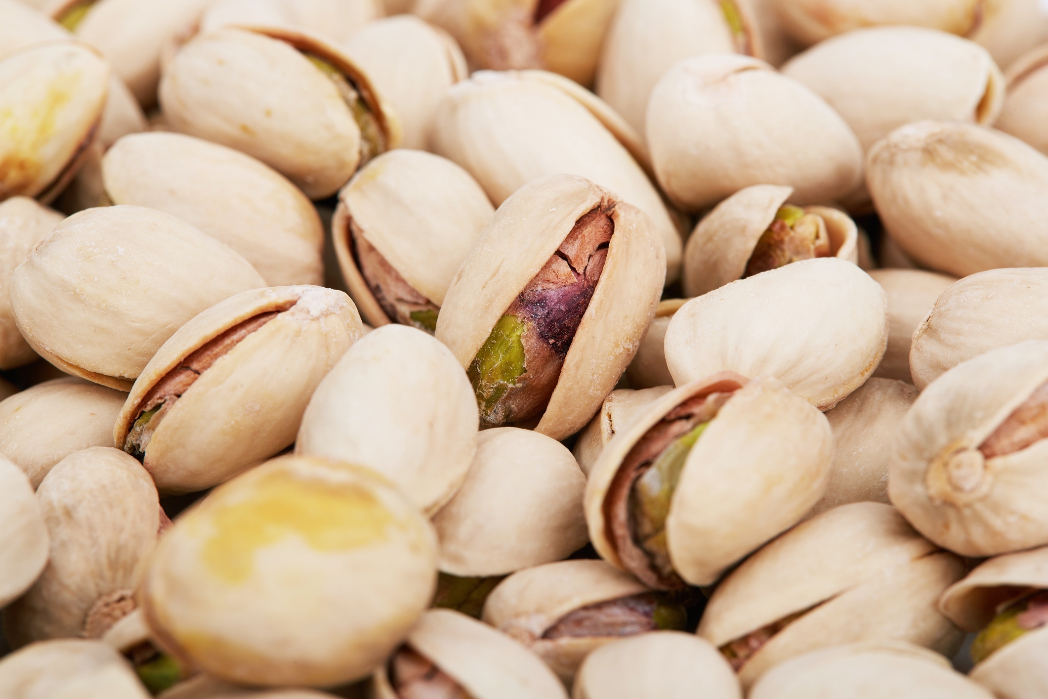 A close-up of several unshelled pistachios scattered, with some shells partially open, revealing the green nuts inside