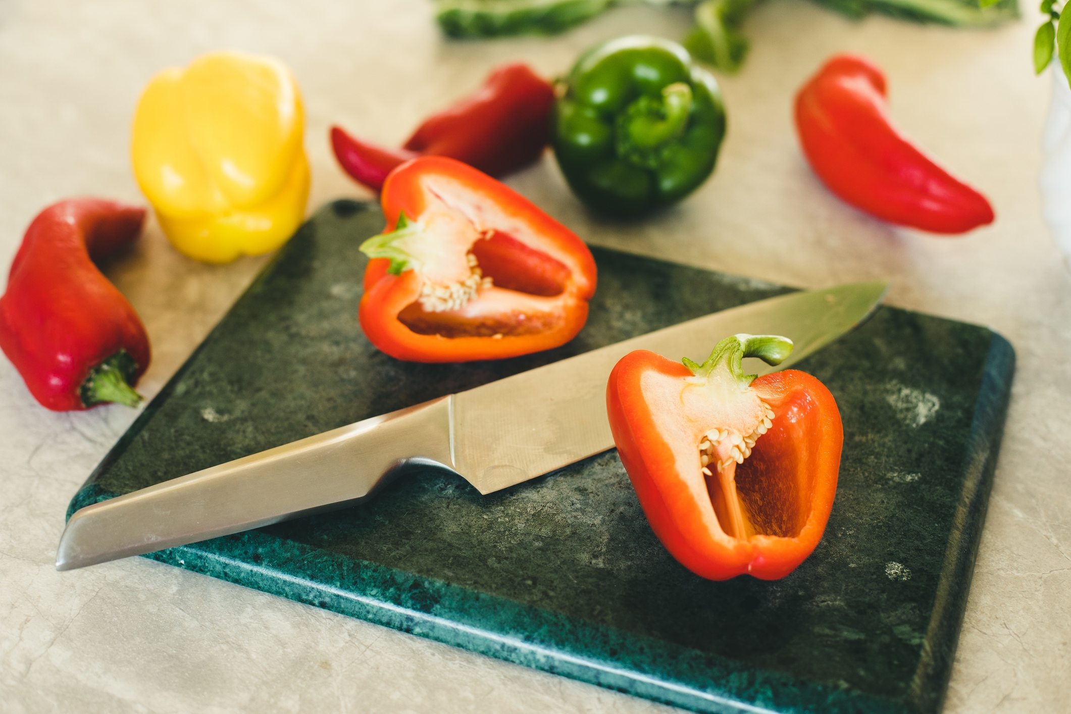 Chopping board with sliced red bell pepper, whole peppers, and a kitchen knife on a counter