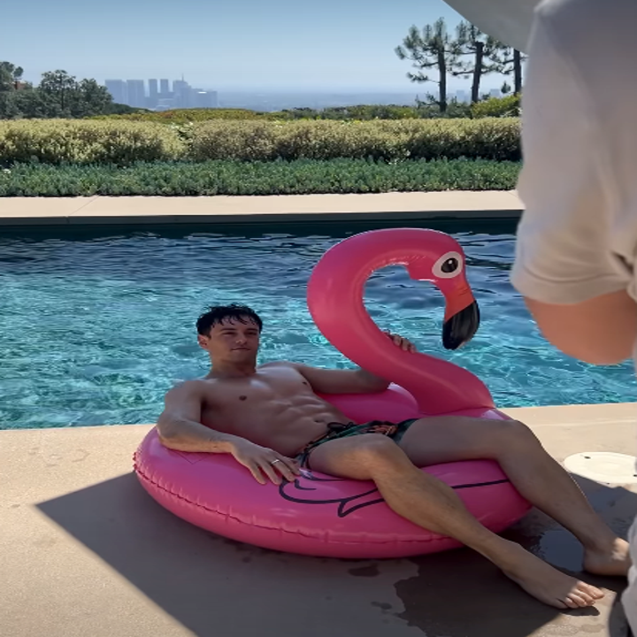 Person relaxing on a flamingo pool floating by a swimming pool, with a picturesque landscape view in the background