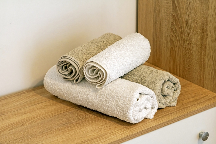 Three neatly rolled towels stacked on a wooden surface, with two beige towels and one white towel on top