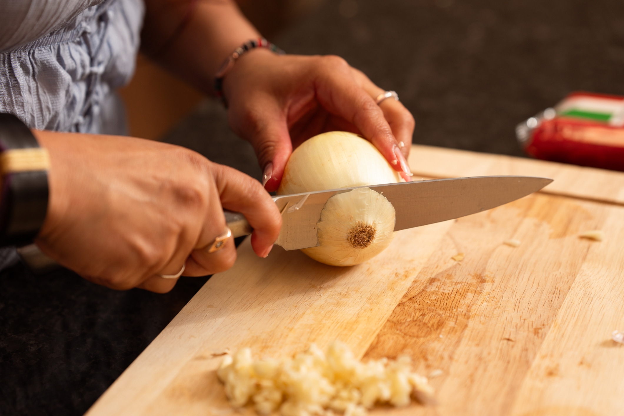 Person cutting an onion on a wooden board with a chef's knife; diced onions nearby