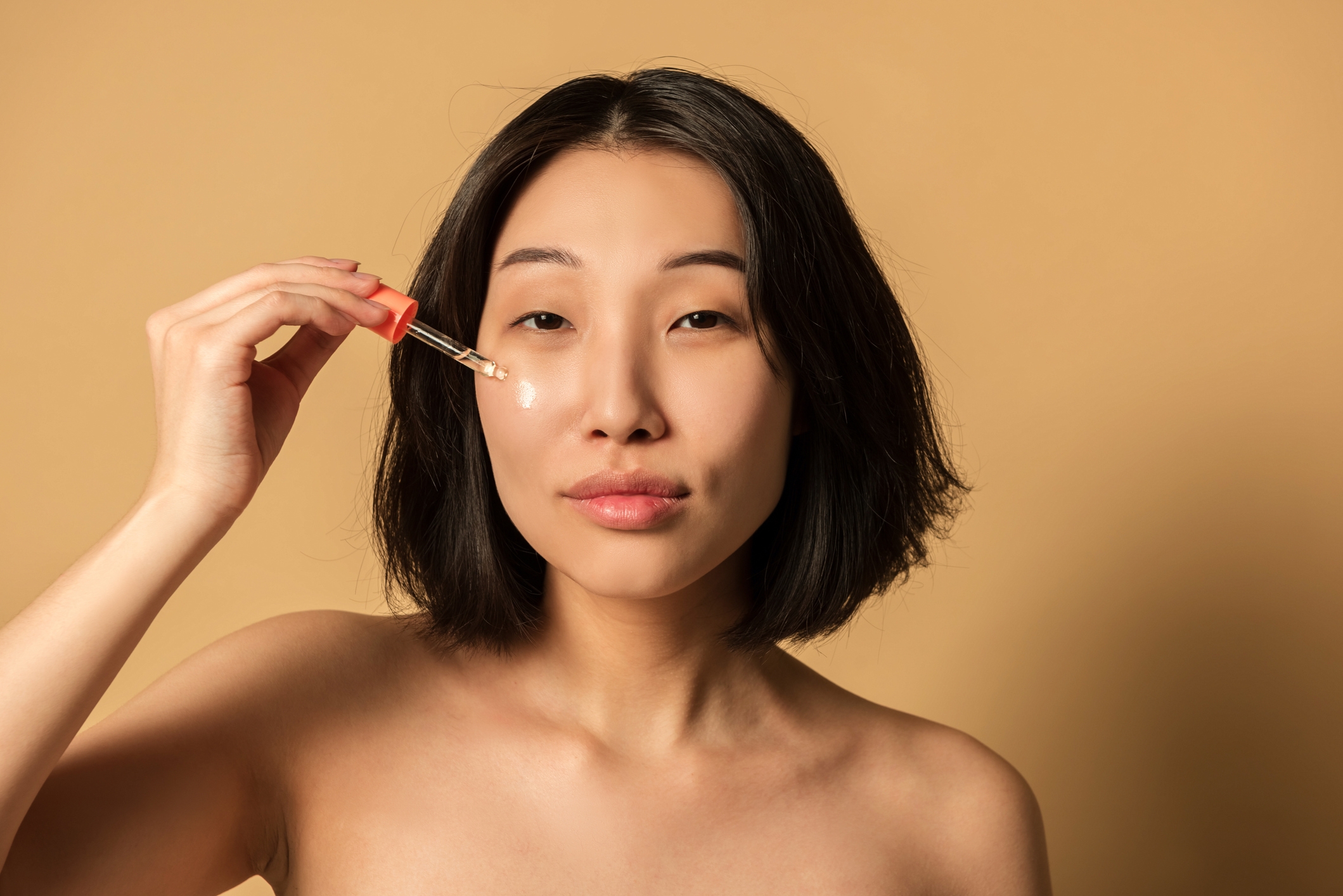 Woman påfører serum i ansiktet med en dropper, og legger vekt på hudpleie i en minimalistisk setting