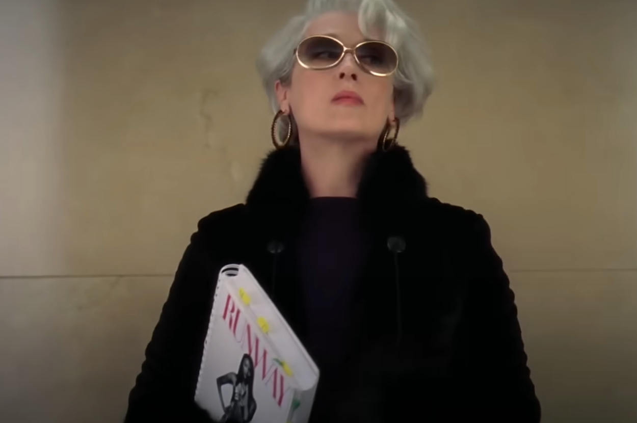 Person wearing sunglasses and a fur-collared coat holds a fashion magazine, embodying a confident and authoritative style