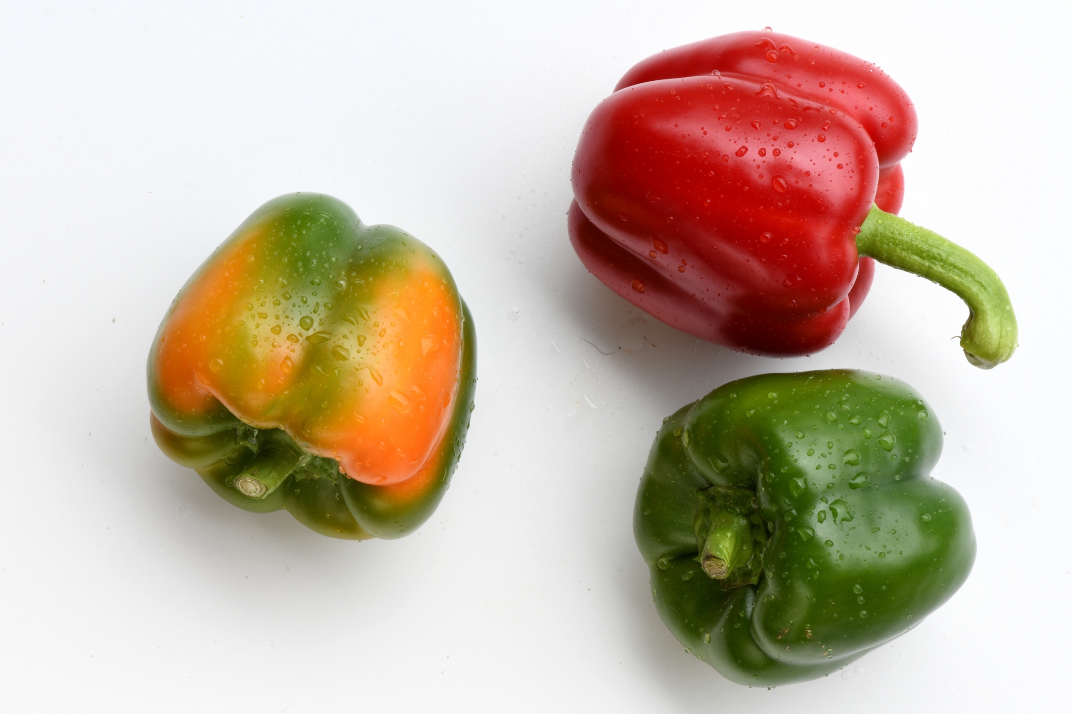 Tre paprika på en hvit bakgrunn, med dråper vann på overflatene