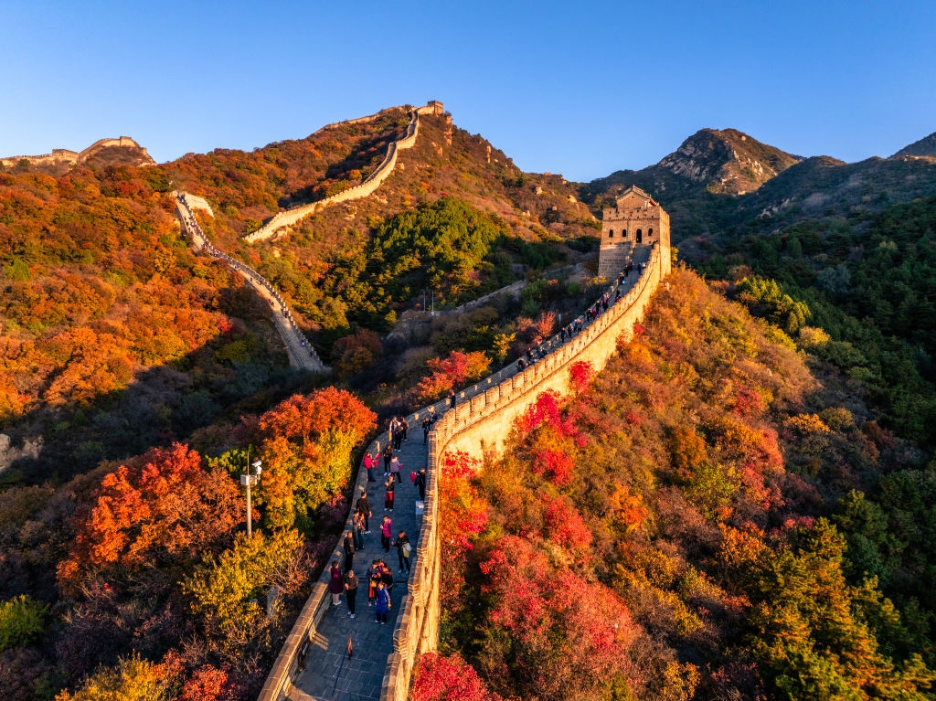 En naturskjønn utsikt over den kinesiske muren som strekker seg over frodig, kupert terreng med turister som går langs stien