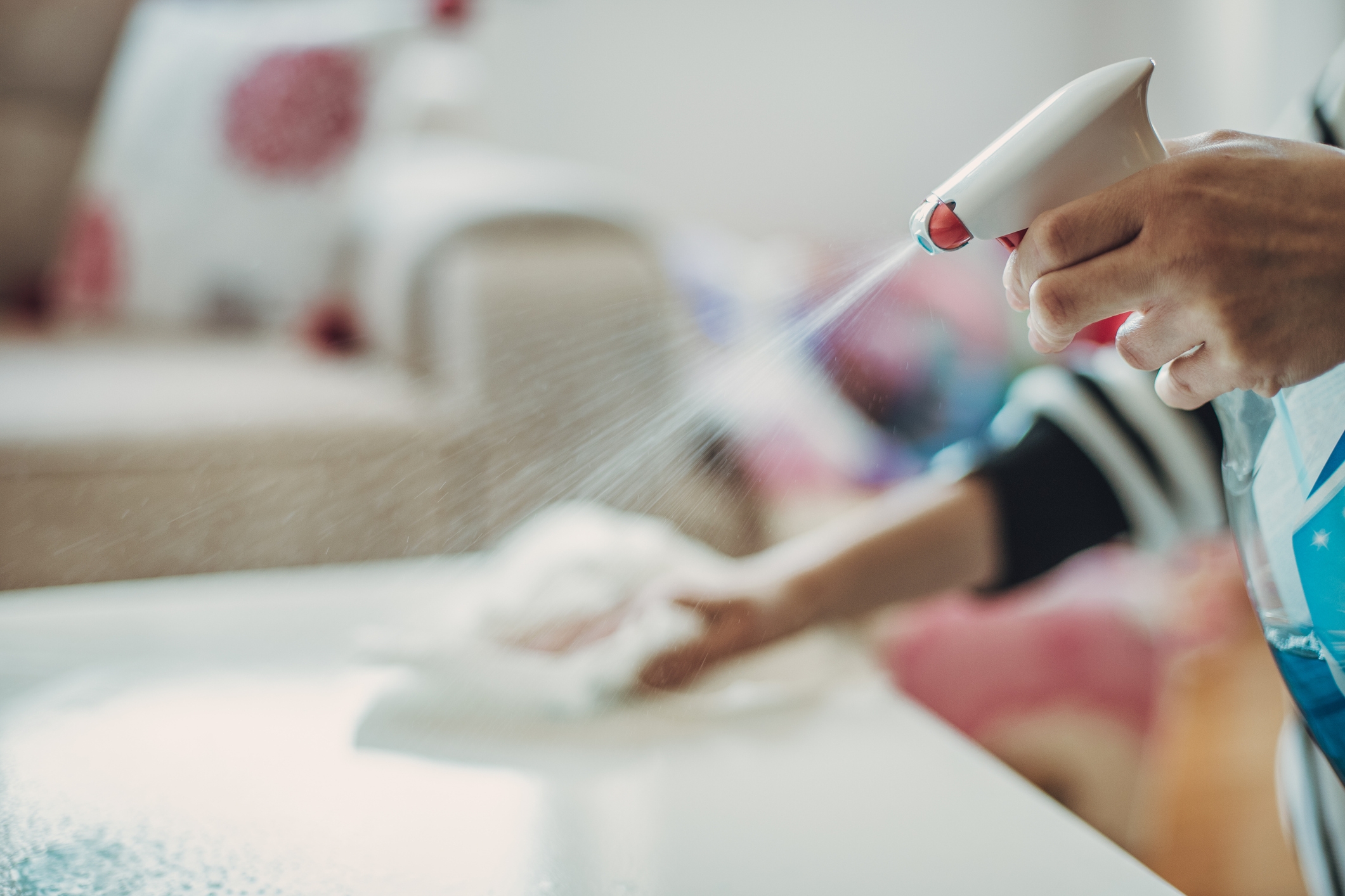 Person sprayer renere på et bord og tørker det med en klut, med fokus på rengjøring og rydding av plassen