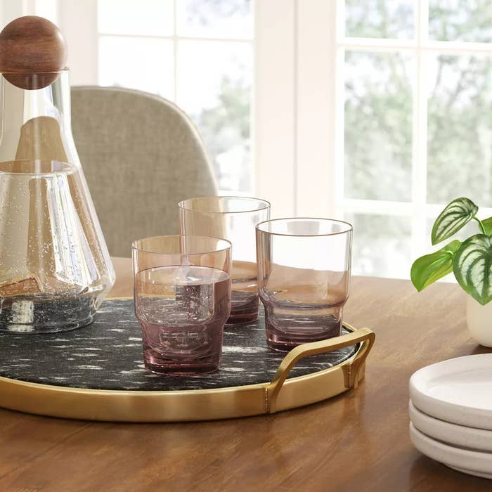 Stylish glassware and carafe acceptable   connected  a circular  tray with a works  and stacked plates, placed connected  a woody  array  by a window