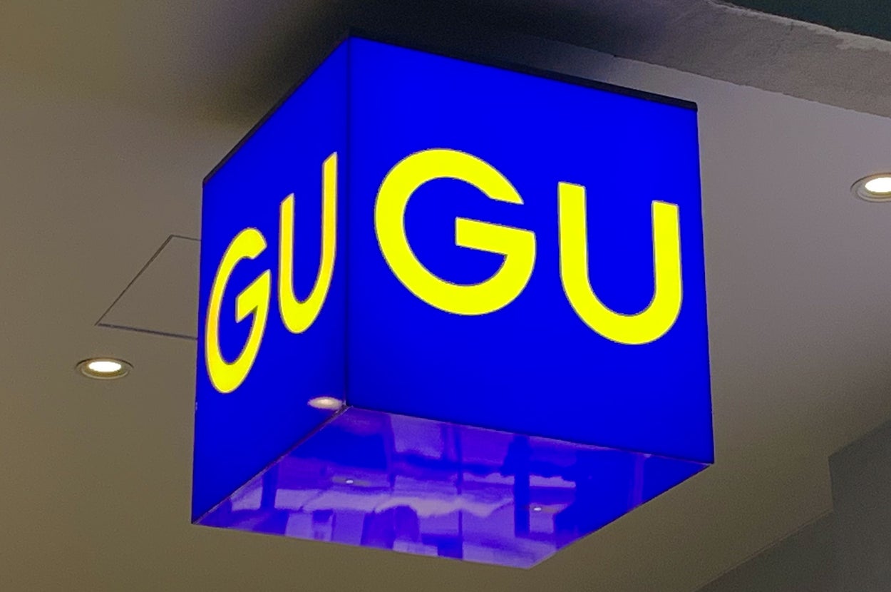 Sign with large yellow letters spelling "GU GU" on a blue cube hanging from the ceiling