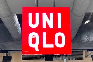 Red Uniqlo sign hangs from a ceiling with visible air ducts in a retail store