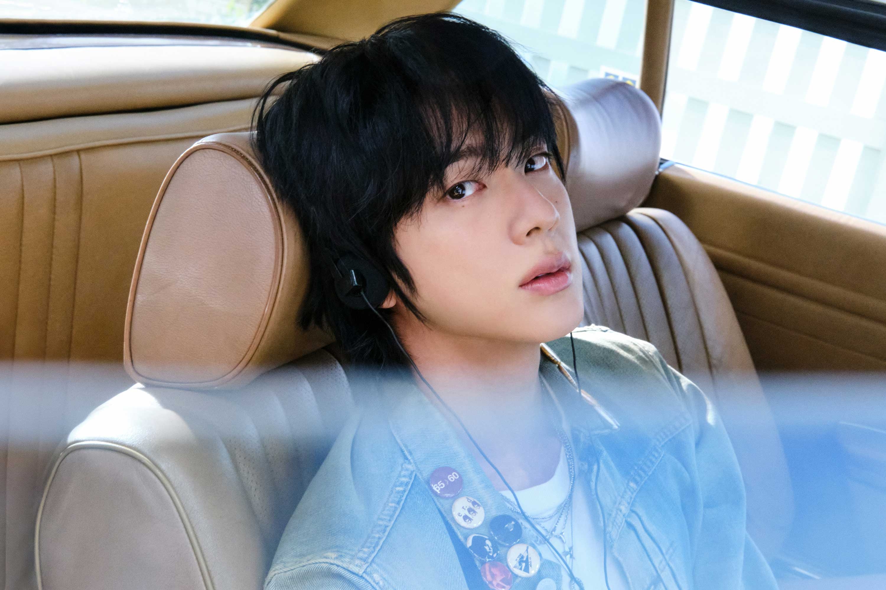 Person with headphones sits in a car seat, gazing thoughtfully out