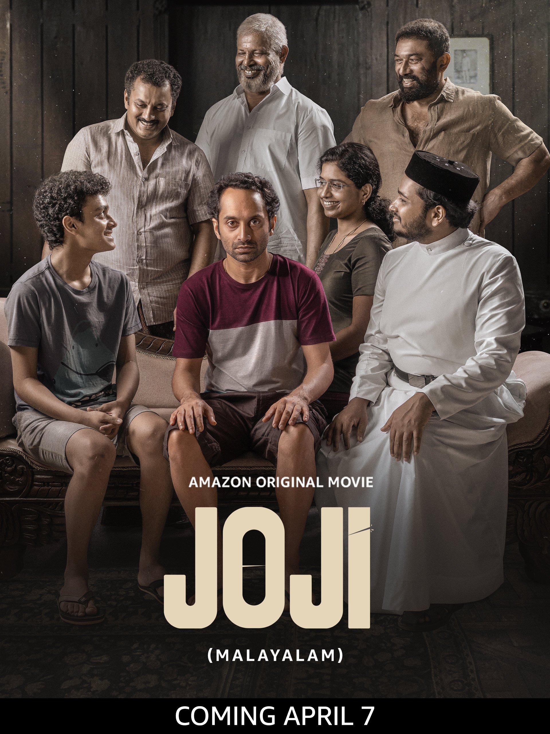 Group of people sitting and standing around a man who is seated on a couch, promoting the Amazon movie "Joji," releasing April 7