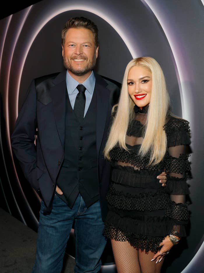 A man in a suit and a woman in a stylish black dress pose together at a music event