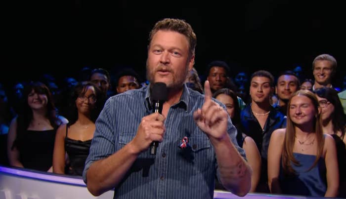 A person holding a microphone speaks to an audience, who are seated and listening attentively