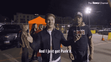 Two people stand in a parking lot at night; the foreground person smiles at the camera, holding a phone with &quot;And I just got Punk&#x27;d&quot; text below