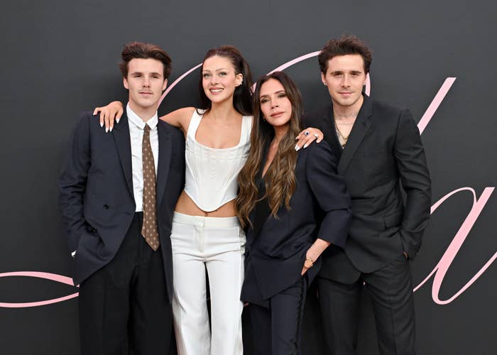 Four people pose together on a red carpet; two men in suits, a woman in a white outfit, and a woman in a dark suit with long hair