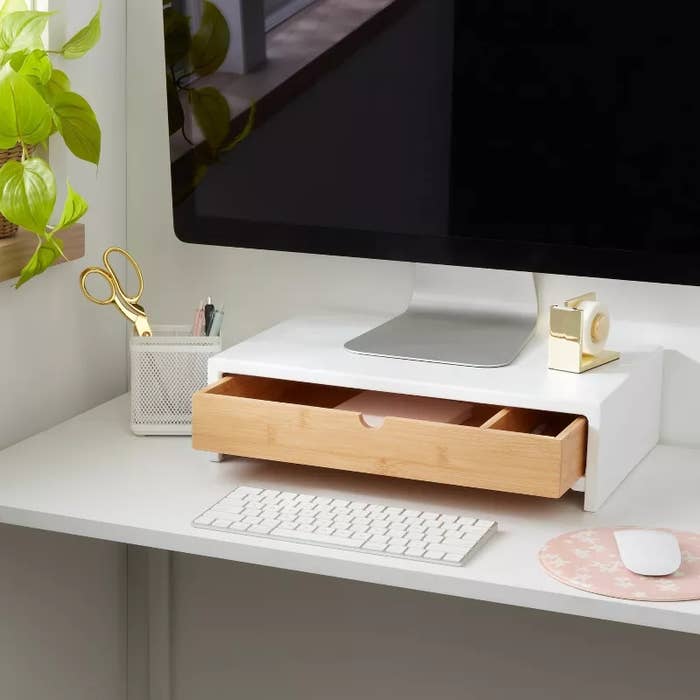 A tidy enactment table with a machine show connected a woody stand, keyboard, rodent pad, plant, scissors, pen holder, and portion dispenser