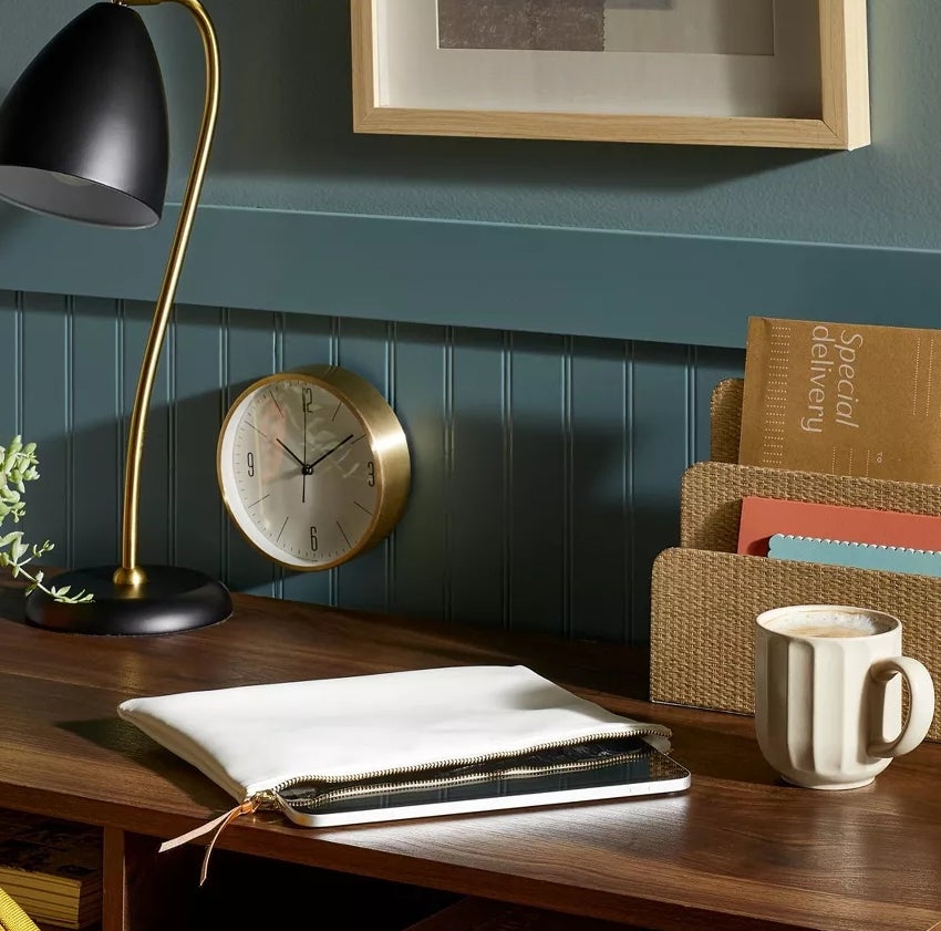 Meja terorganisir dengan lampu, jam, tanaman, buku catatan, mug, dan tempat arsip di permukaan kayu di bawah seni berbingkai