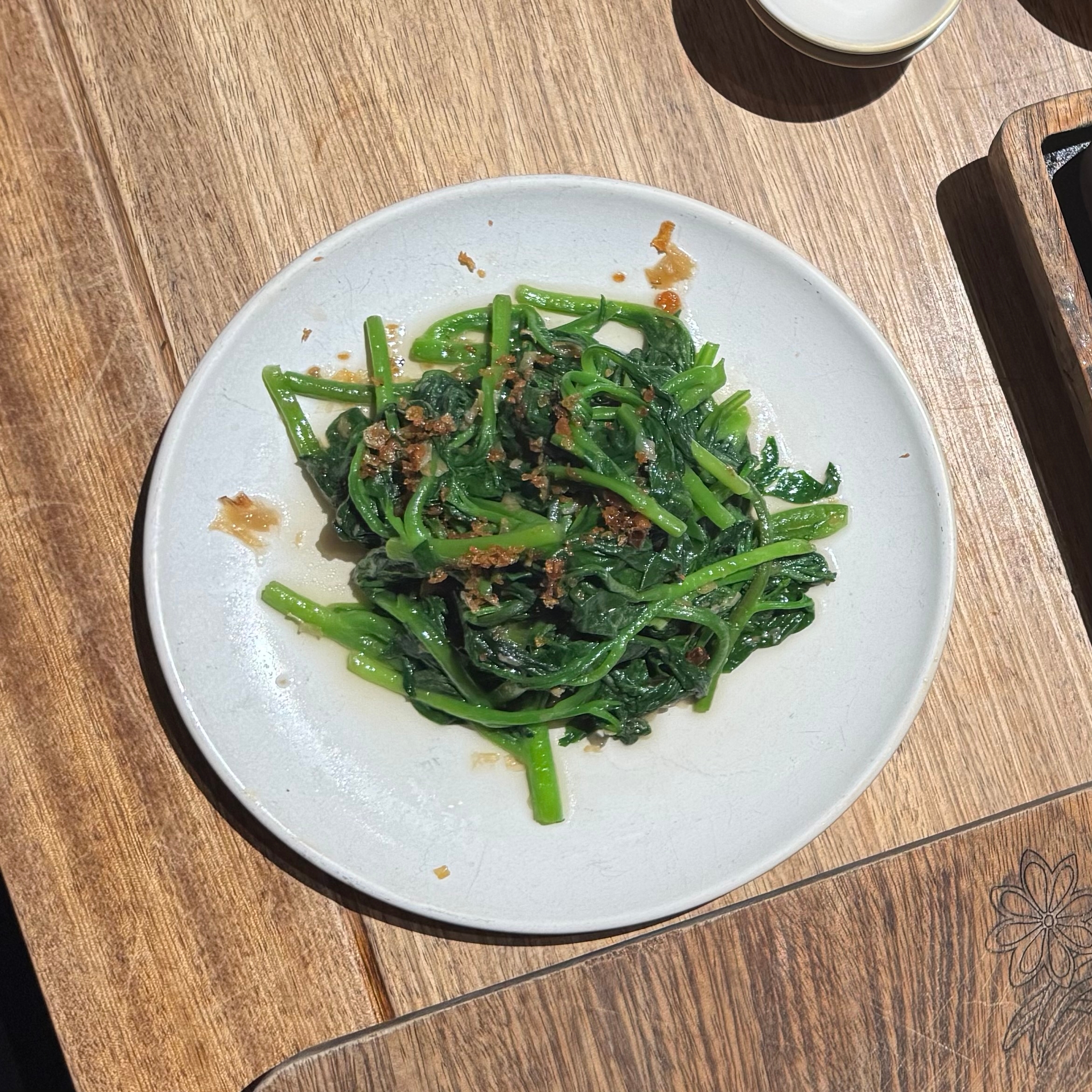 Plate of sautéed greens with crispy shallots on a wooden table