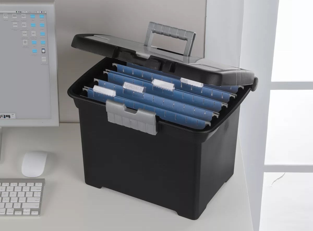 Meja kantor dengan komputer dan kotak file terbuka menampilkan folder terorganisir dengan tab