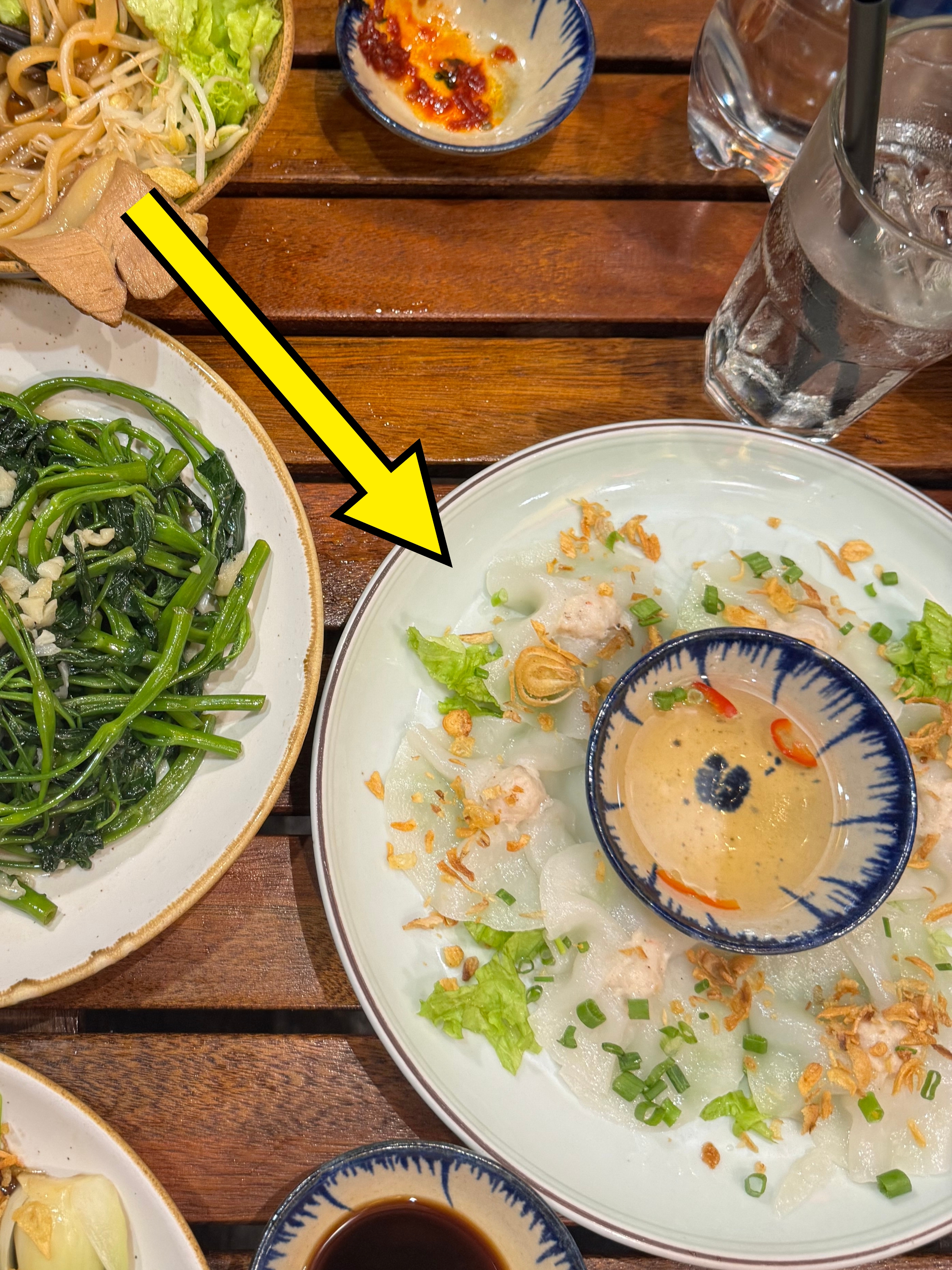A table with plates of various Vietnamese dishes, including sautéed greens, rice with pork, vermicelli, lettuce, and dipping sauces