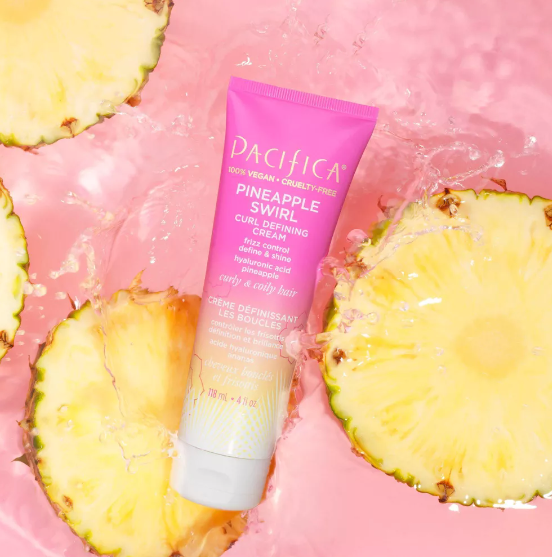 Pacifica Pineapple Swirl Curl Cream Tube Dikelilingi oleh Irisan Nanas Dengan Latar Belakang Merah Muda