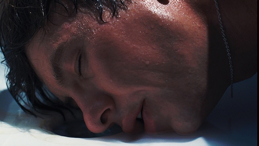 Person with wet hair resting their face on a reflective surface, eyes closed, with a serene expression