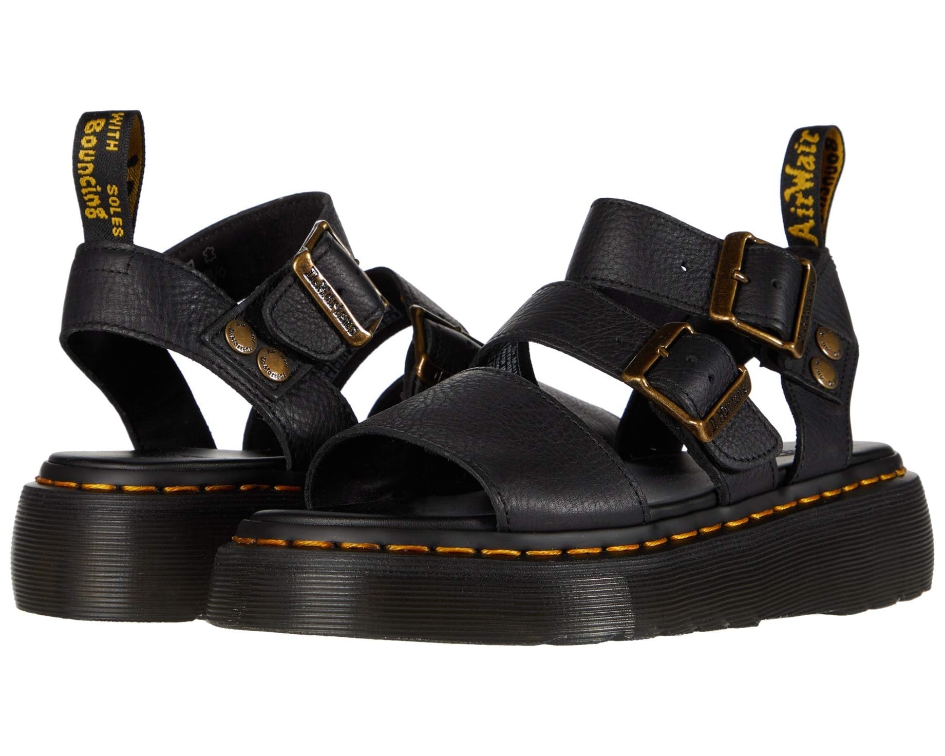 Pair of chunky black sandals with thick soles and buckle straps, featuring distinctive yellow stitching