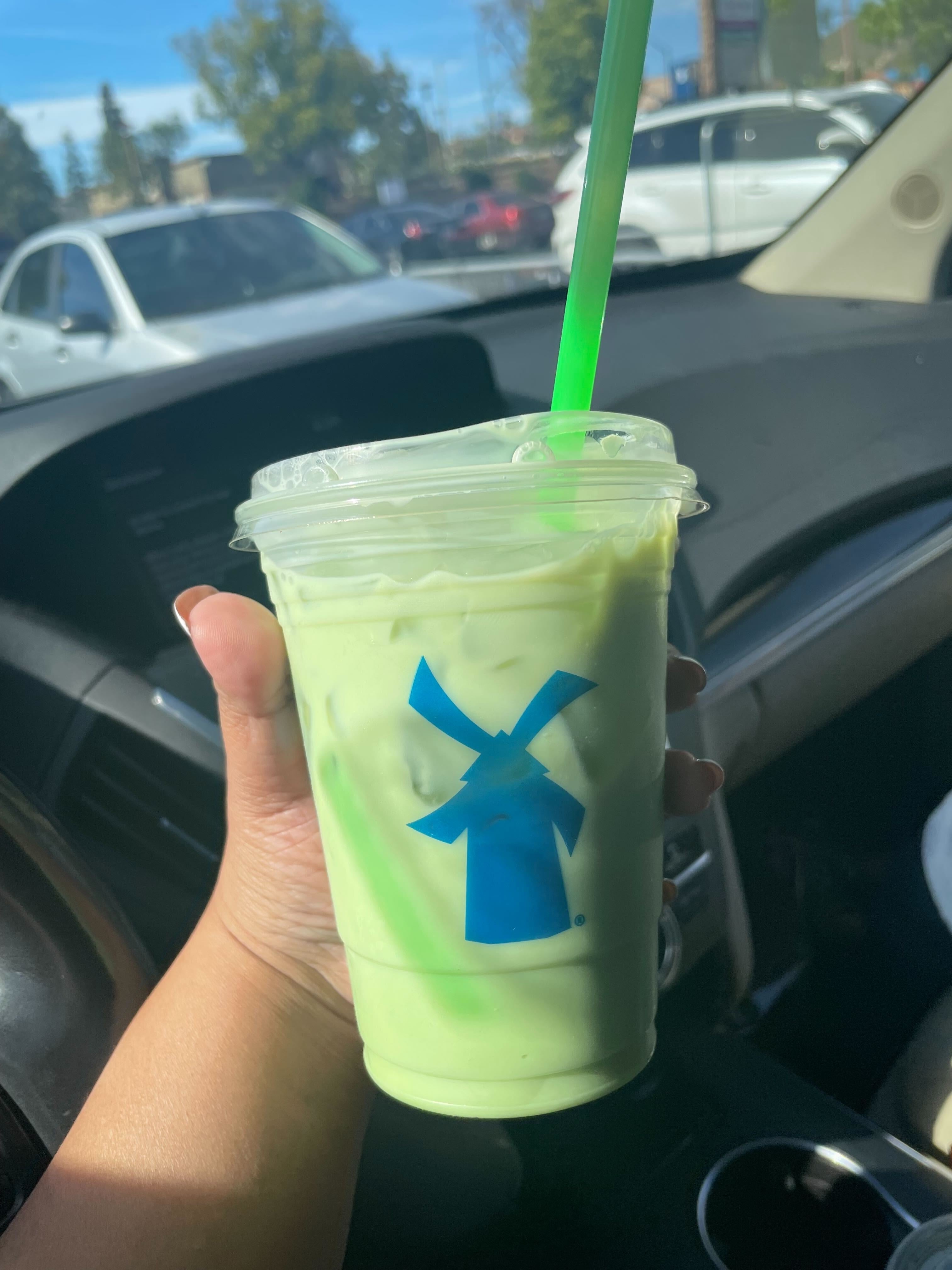 Person holding an iced green drink in a clear plastic cup with a green straw, inside a car