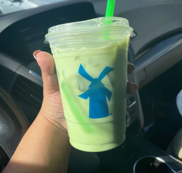 Person holding an iced green drink in a clear plastic cup with a green straw, inside a car