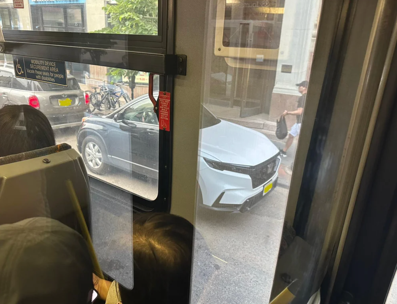 View from a bus window showing a car blocking the street, with passengers inside the bus looking out