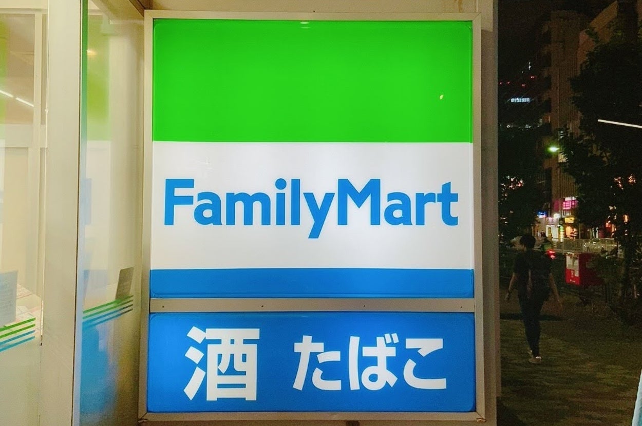 ファミリーマートの看板。店名の下に「酒 たばこ」の文字が表示されています。夜の街並みが背景に映っています。