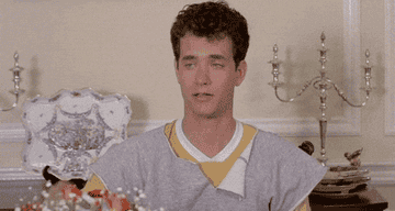 Person sitting at a dining table looking unimpressed. They&#x27;re wearing layered casual clothing with a white collar showing