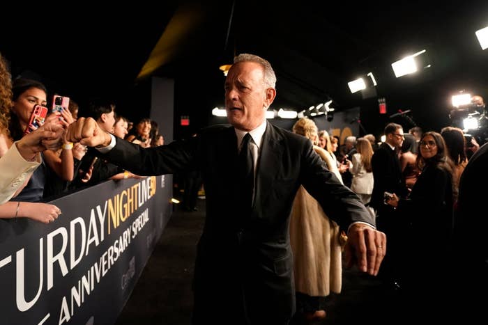 Actor in a black suit greets fans at an event, posing for photos and interacting on a crowded red carpet