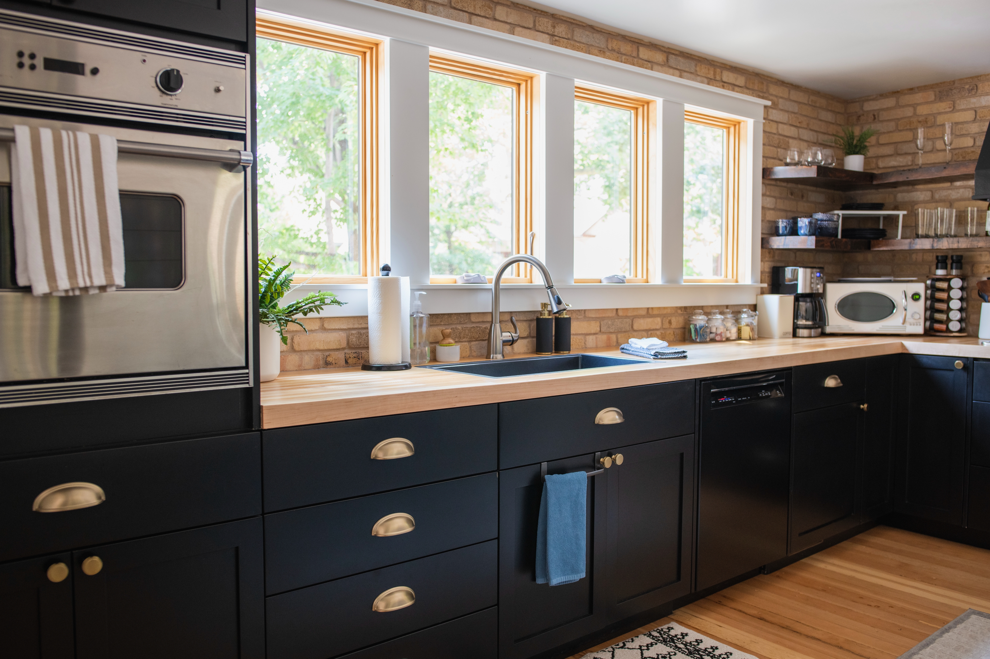 Modern kitchen with black cabinets, wooden countertops, stainless steel oven, and large windows providing natural light.