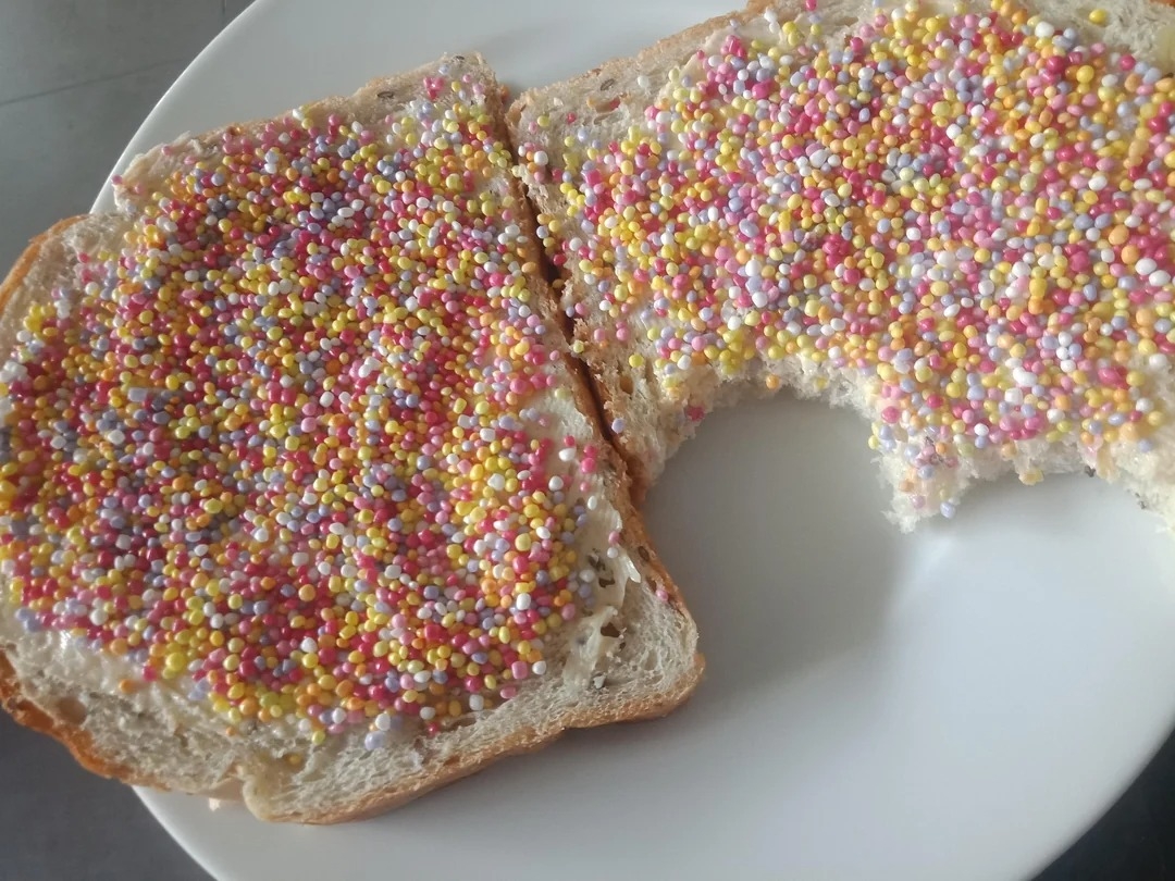 Slice of bread with butter and colorful sprinkles, partially eaten, on a white plate
