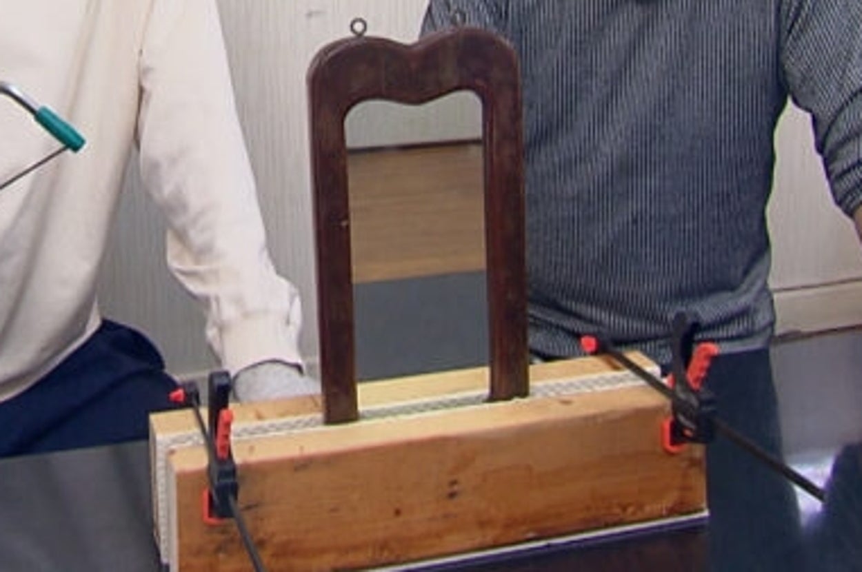 2人の男性が室内でミラー修繕に取り組んでいる。1人は工具を手に持ち、もう1人は作業を見守っている。