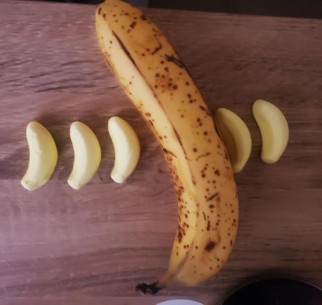 A large ripe banana surrounded by several banana-shaped candies on a wooden surface