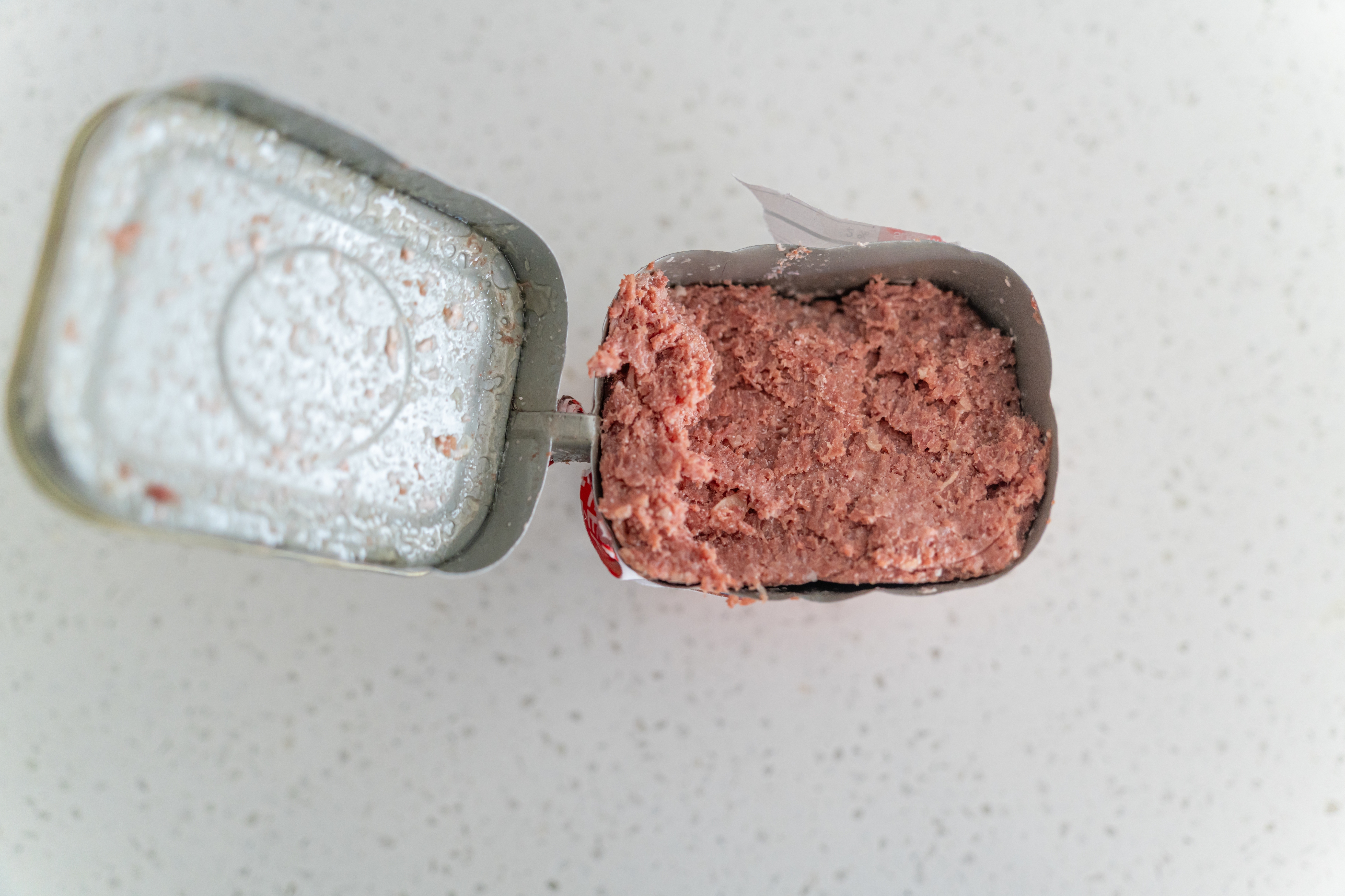 Open can with processed meat on a speckled countertop