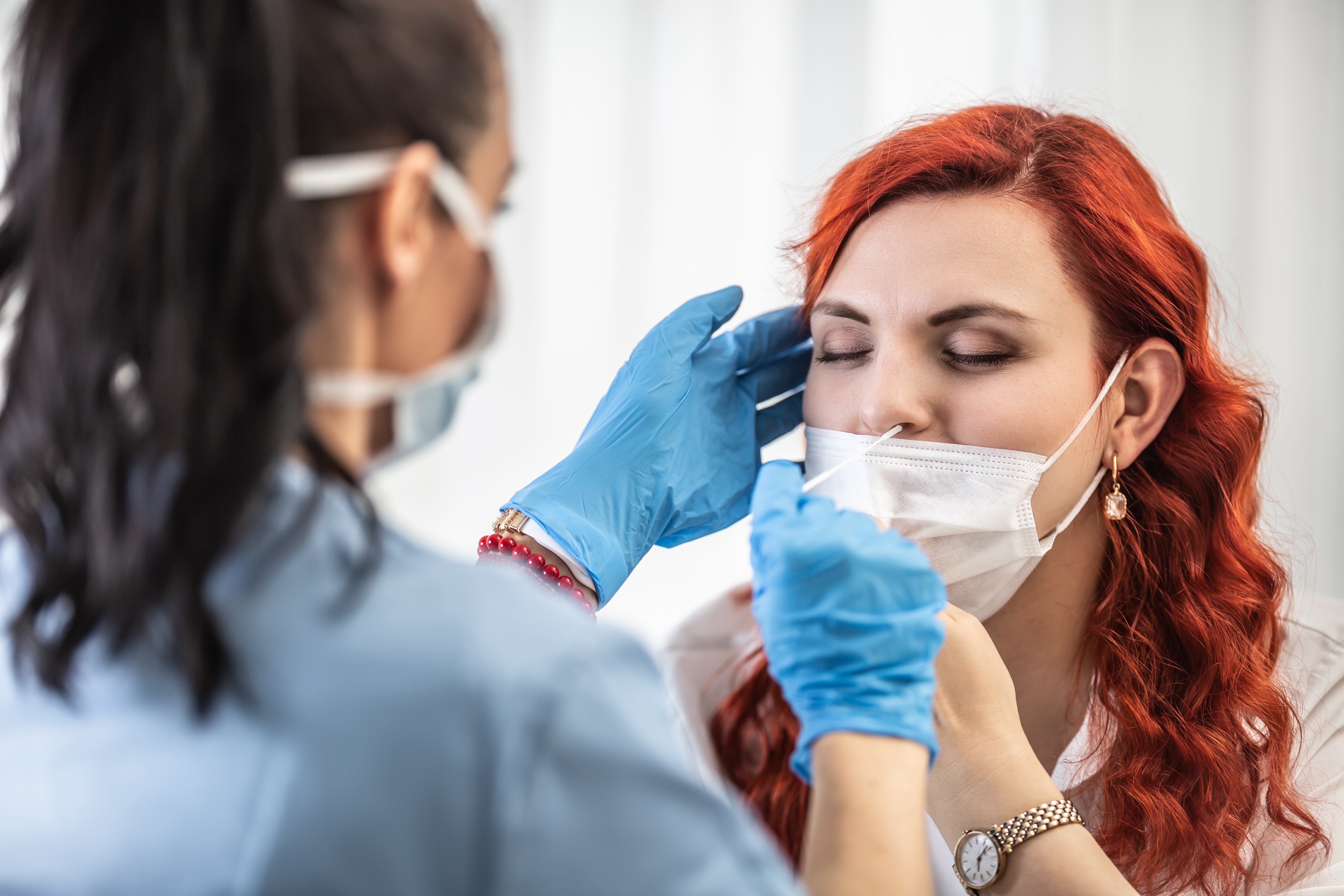 Healthcare worker administers a nasal swab test to a woman with red hair wearing a mask, highlighting COVID-19 safety testing measures